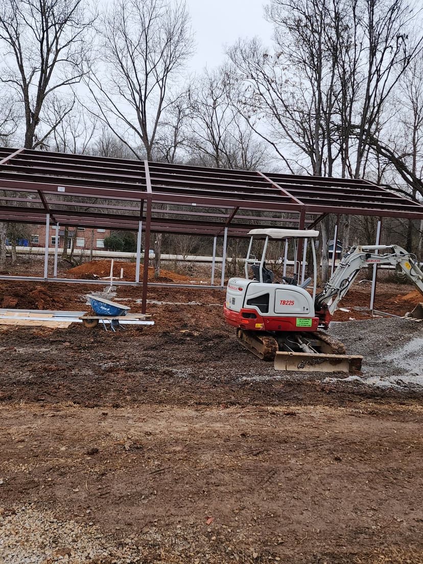 Steel frame construction site with machinery and tools in a clearing surrounded by trees.